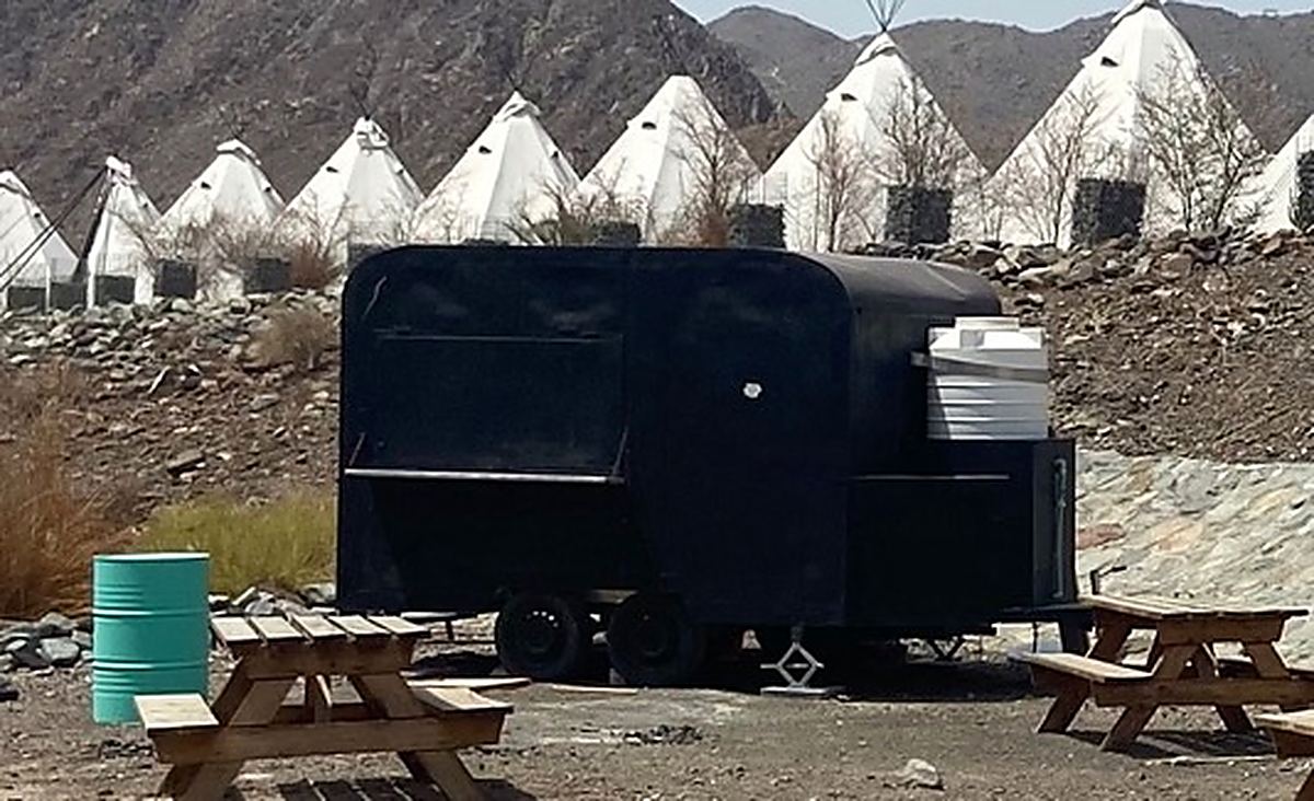 A black food truck parked in front of a row of teepees with picnic benches